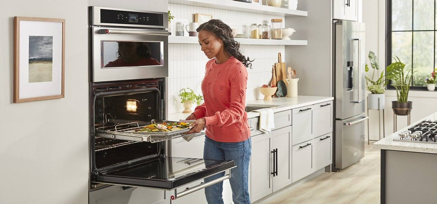 A woman pulling a dish of baked vegetables out of a combination wall oven