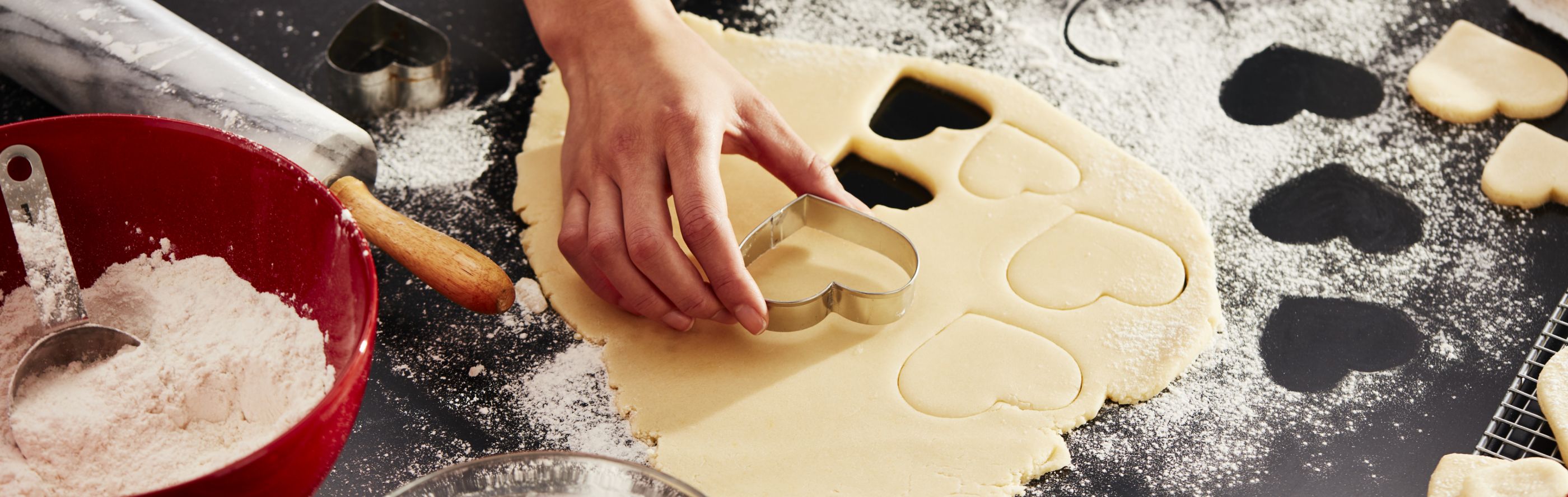 A piece of dough being pressed with a cookie cutter, surrounded by other baking instruments