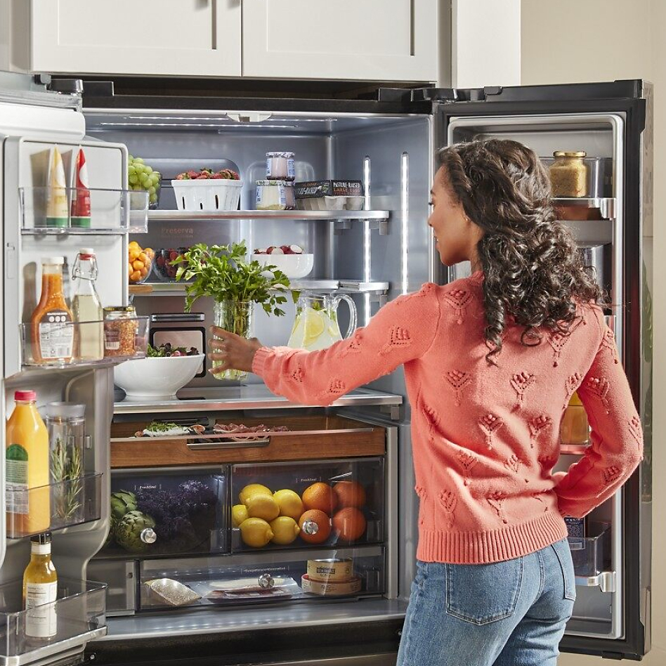 Woman in pink sweater putting herbs in French door type of refrigerator
