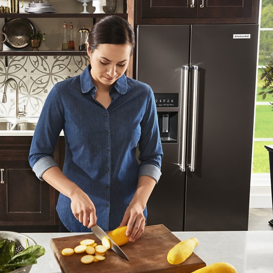 Woman preparing food in front of side-by-side fridge type in modern kitchen