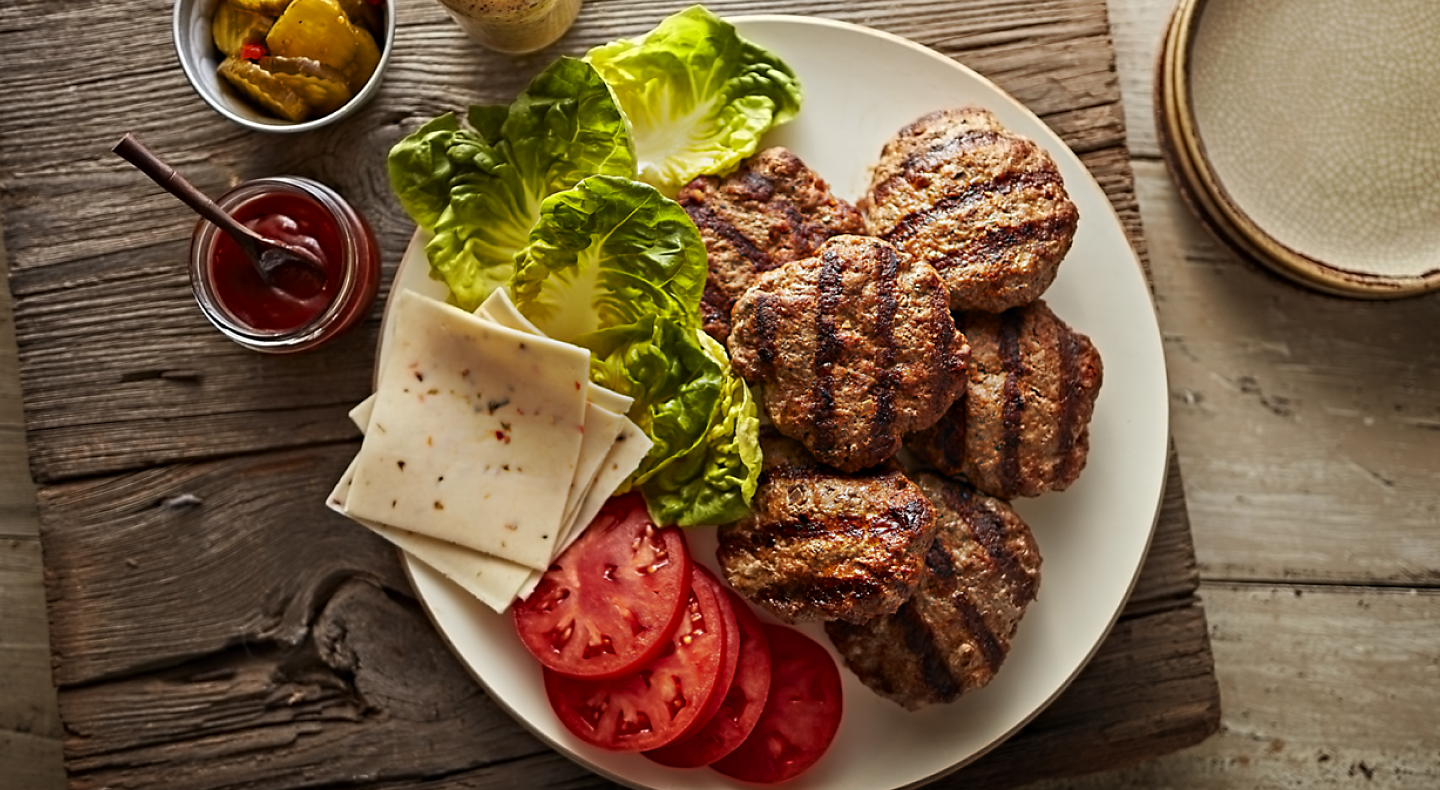 Grilled burger patties on a plate with toppings and sauces