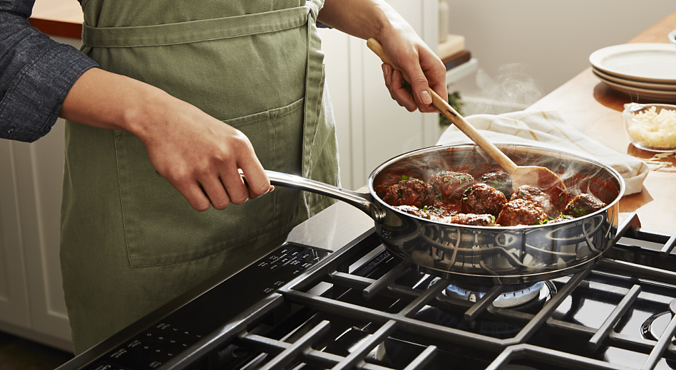 A person simmering meatballs on a stovetop