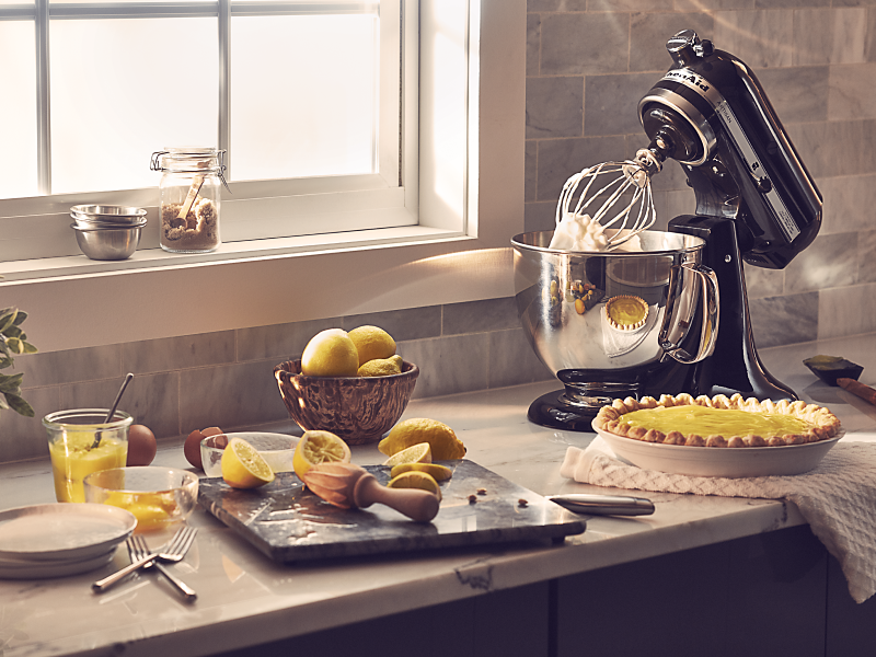 Black KitchenAid® stand mixer on countertop next to lemon custard pie with other baking ingredients