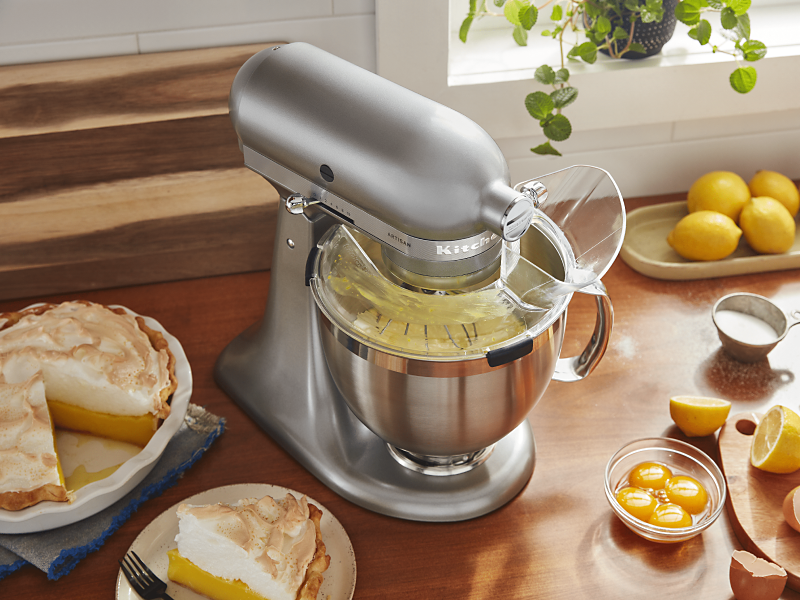 Silver KitchenAid® stand mixer with Pour Shield on countertop with lemon meringue pie and ingredients