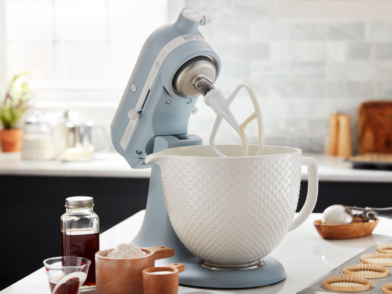 A KitchenAid® stand mixer with a flat beater accessory on the counter of a modern kitchen.
