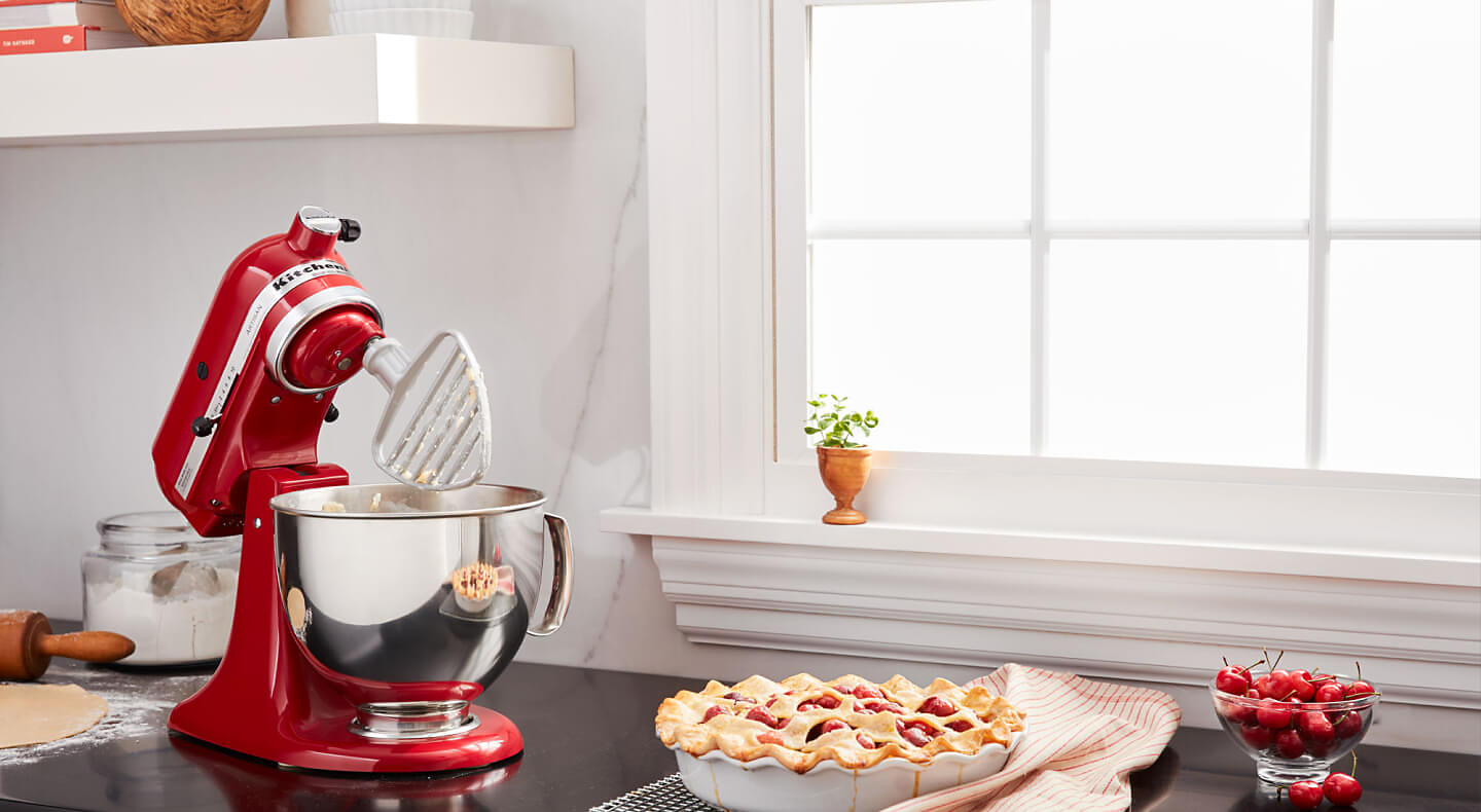 A KitchenAid® stand mixer with a pastry beater accessory next to a pie on the counter of a modern kitchen.