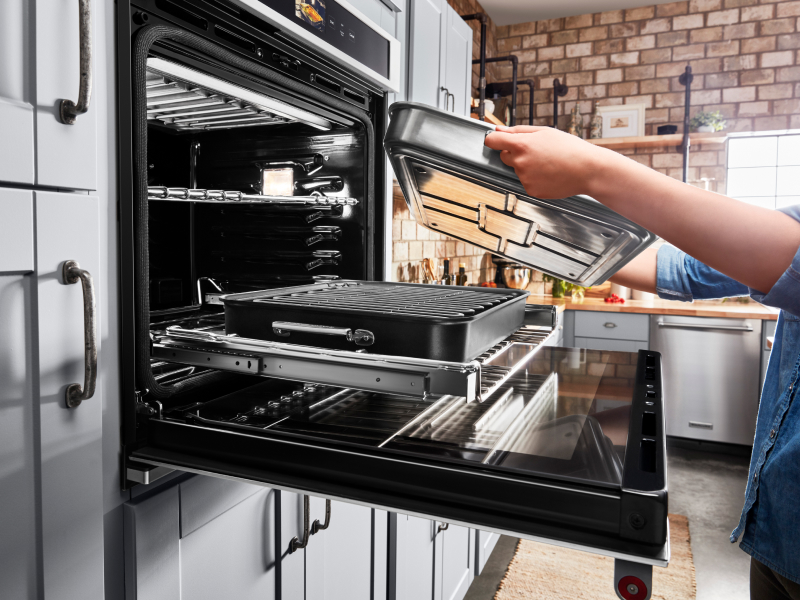A person placing a baking pan on the roll-out tray of a KitchenAid® Smart Oven+