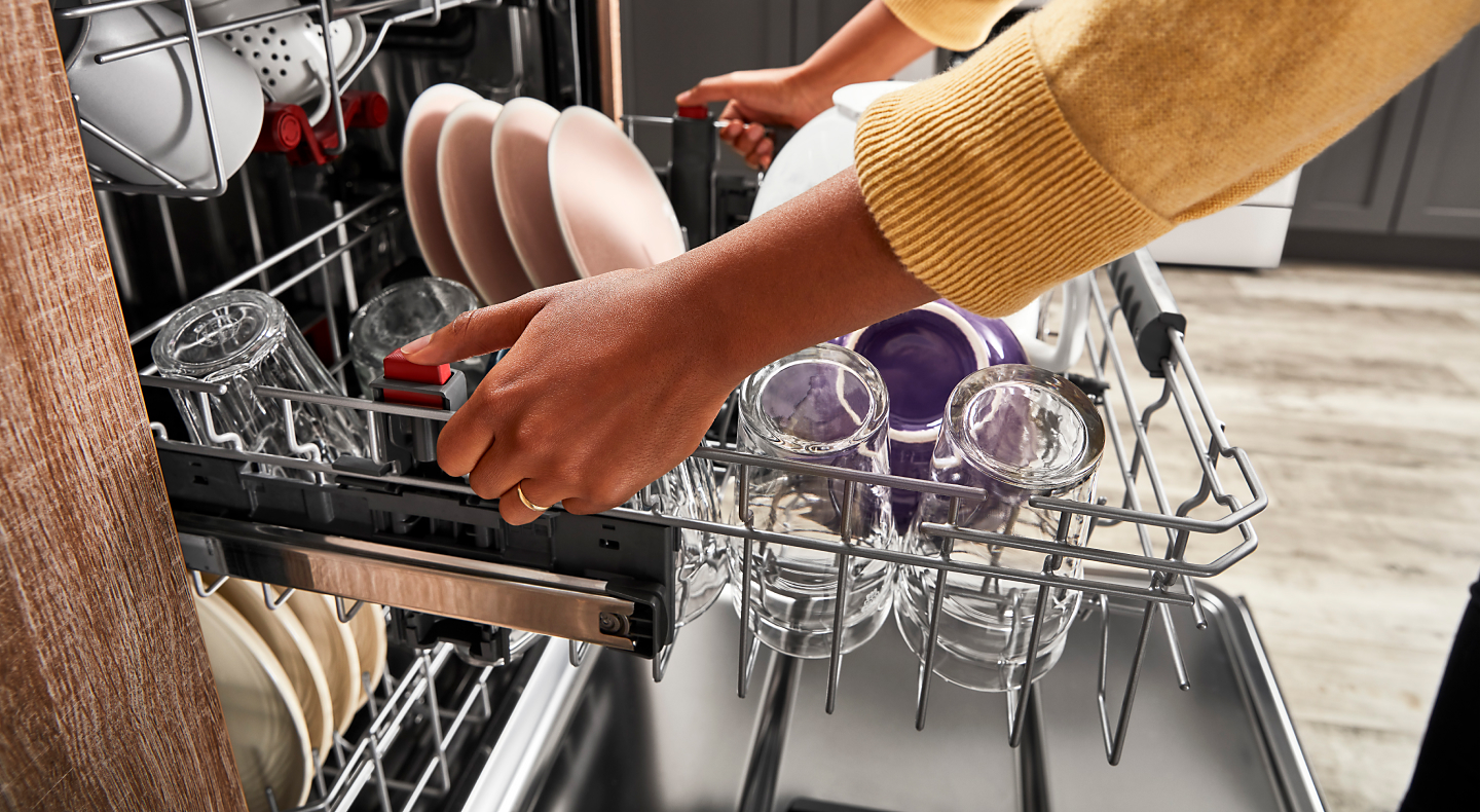 Woman pulling out a dishwasher rack filled with cups and plates