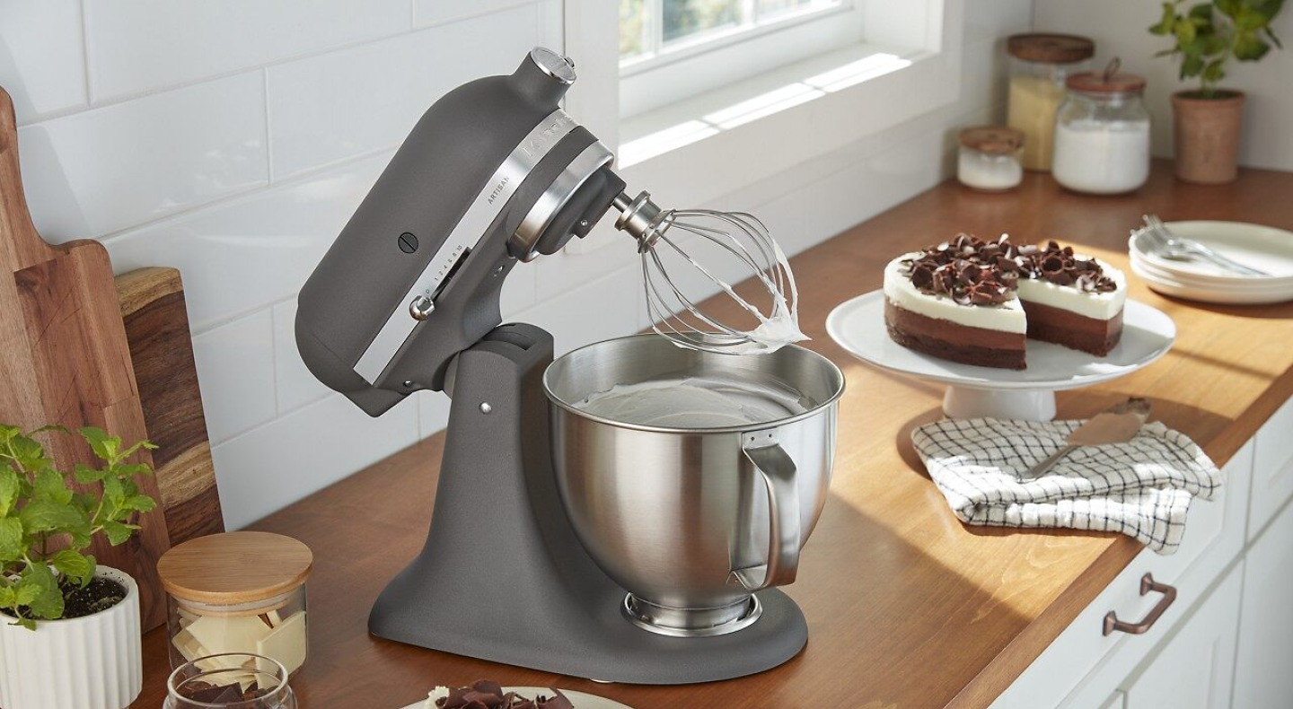 A black KitchenAid® stand mixer next to a cake on a counter.