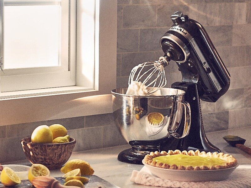 A black KitchenAid® stand mixer next to a lemon pie and lemon slices.