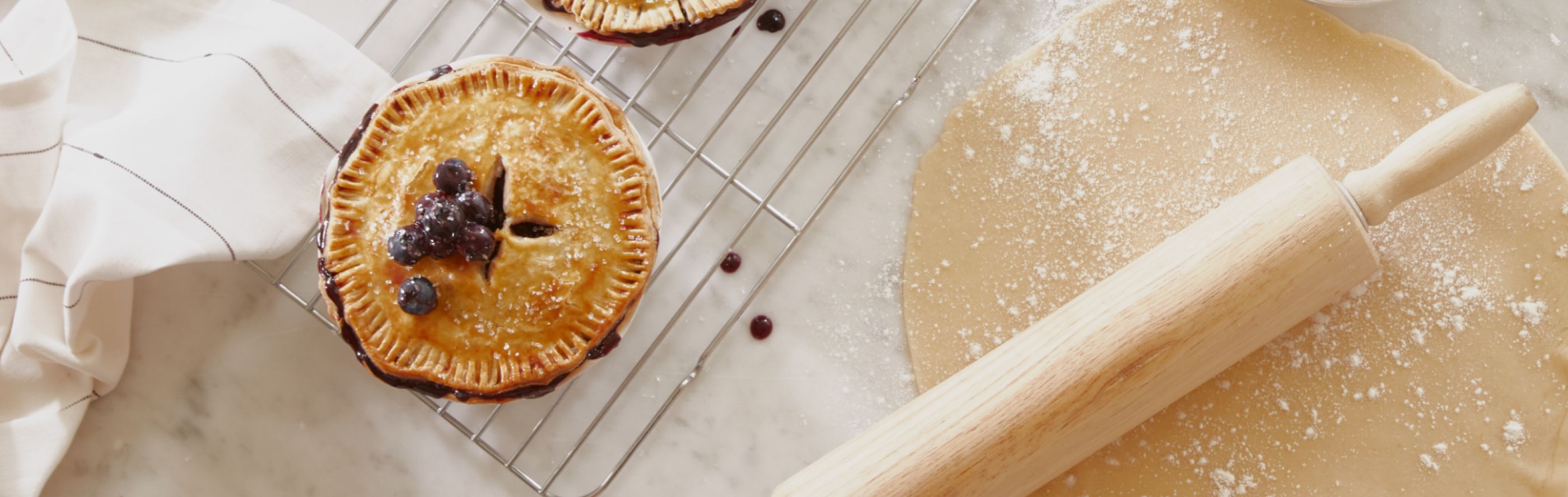 A blueberry pie next to a rolling pin and flour.