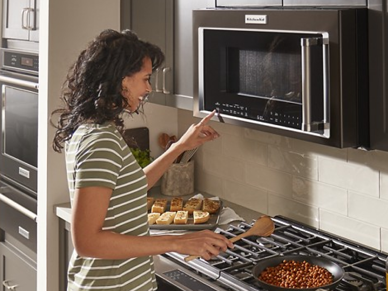Woman cooking on a stove and selecting a cook setting on a KitchenAid® microwave