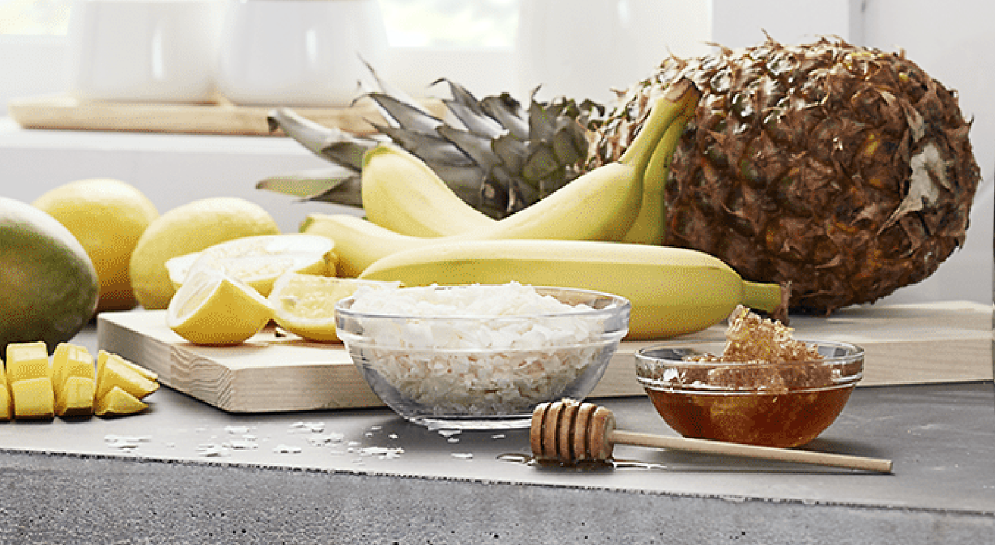 Pineapple, mango, lemon, banana, coconut flakes and honey on the countertop of a modern kitchen. 