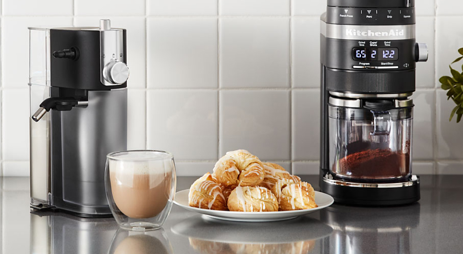 A cup of whipped coffee on a stainless steel countertop with baked goods and appliances