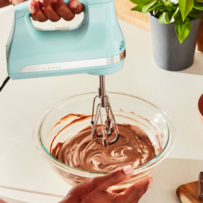 A person mixing chocolate icing with a corded hand mixer