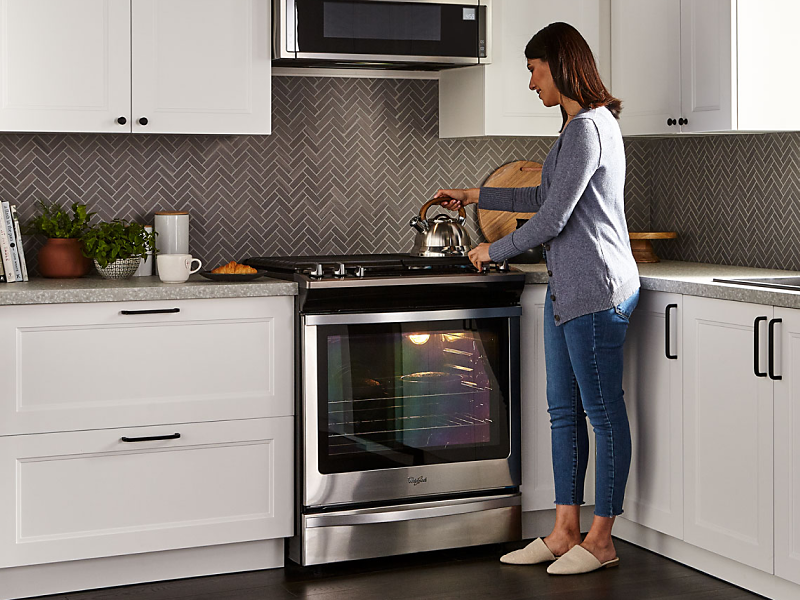 A woman standing next to a Whirlpool® oven in a modern kitchen.