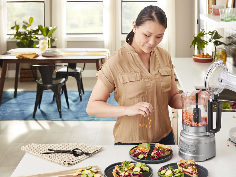 Woman placing carrots grated in KitchenAid® food processor on salad
