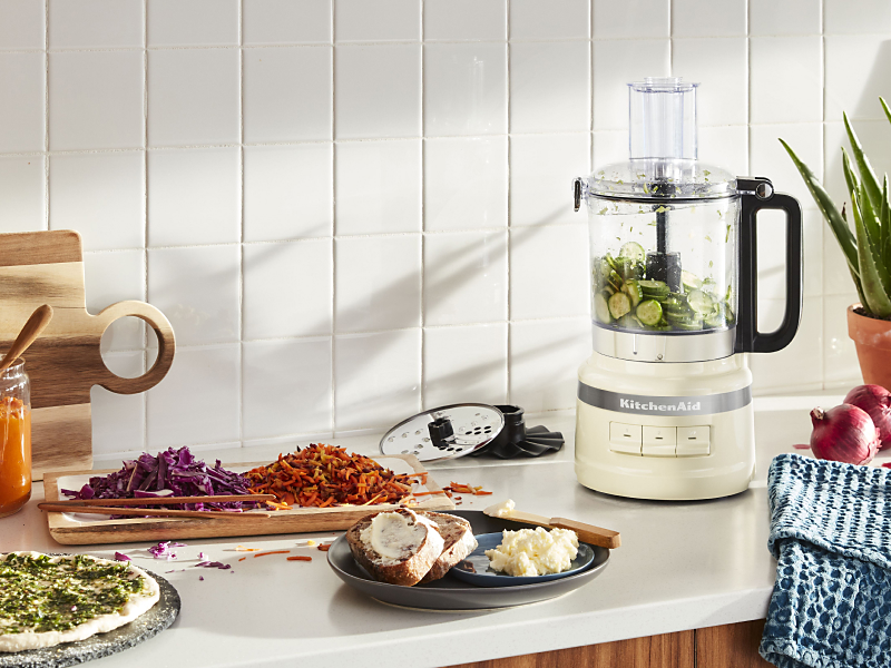 KitchenAid® food processor with grated zucchini and homemade pizza ingredients