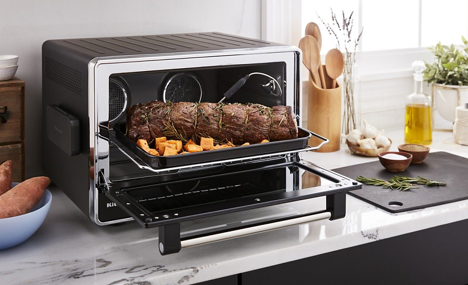 Open KitchenAid countertop oven with roasted meat and sweet potatoes on rack