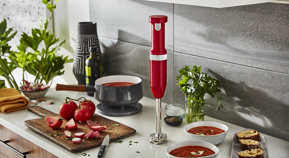 Red KitchenAid® Cordless Variable Speed Hand Blender with bowls of tomato soup