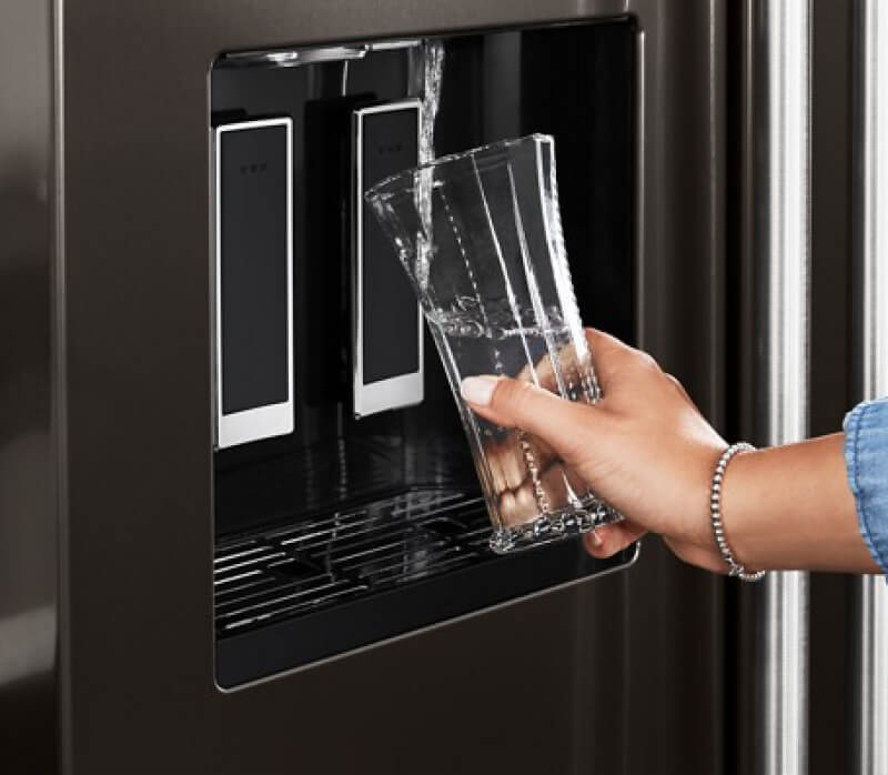 A person filling water from an external dispenser of the KitchenAid® French Door Bottom Mount Refrigerator.