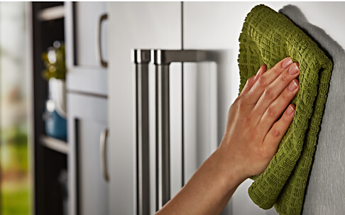 A person using a soft cloth to wipe the exterior of the KitchenAid® French Door Bottom Mount Refrigerator.