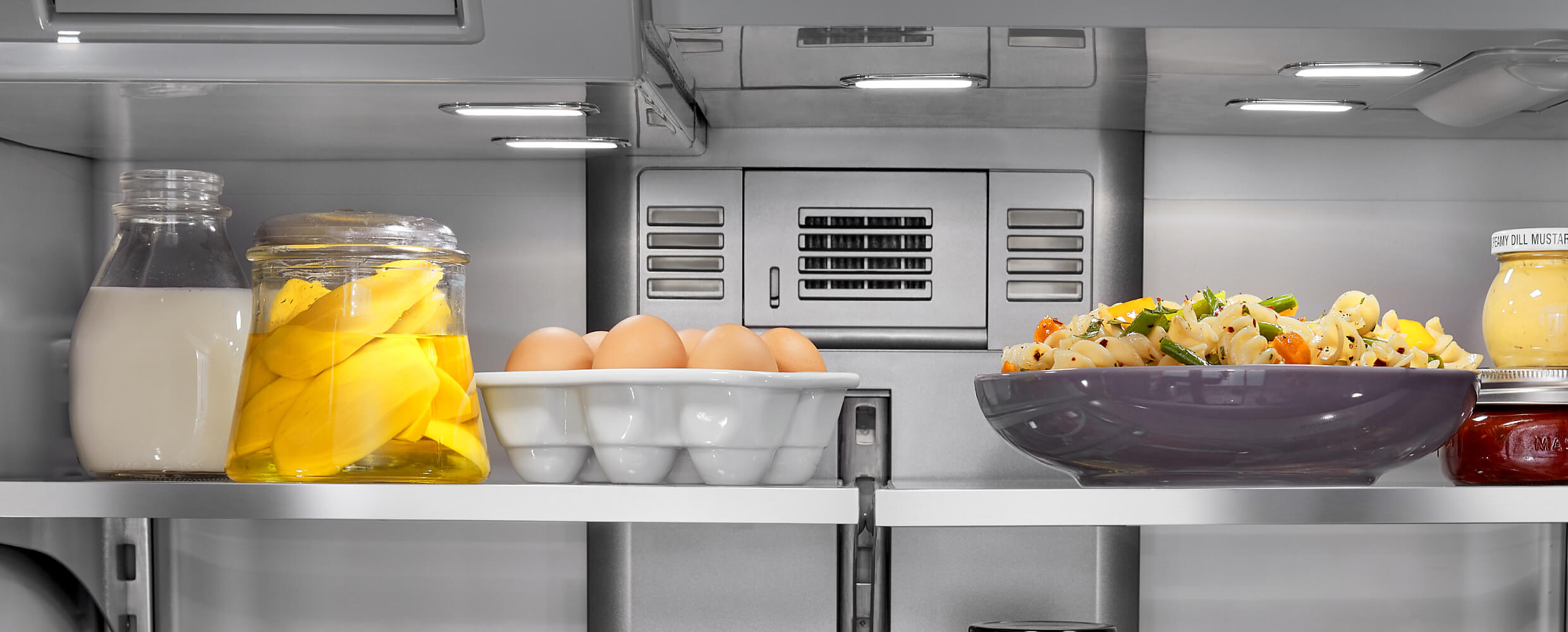 The top shelf of the KitchenAid® French Door Bottom Mount Refrigerator filled with different fresh foods, eggs and milk. 