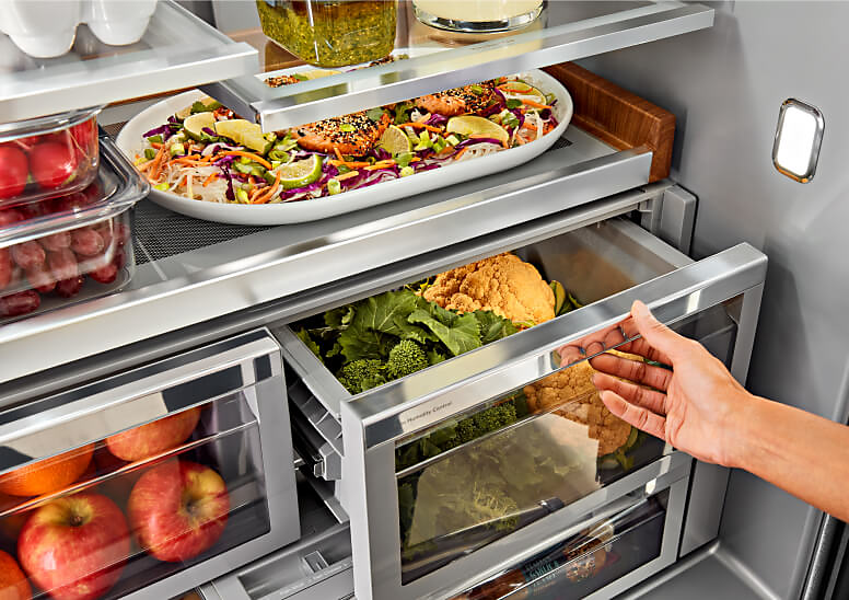 A person opening a fully stocked produce drawer in the KitchenAid® French Door Bottom Mount Refrigerator. 