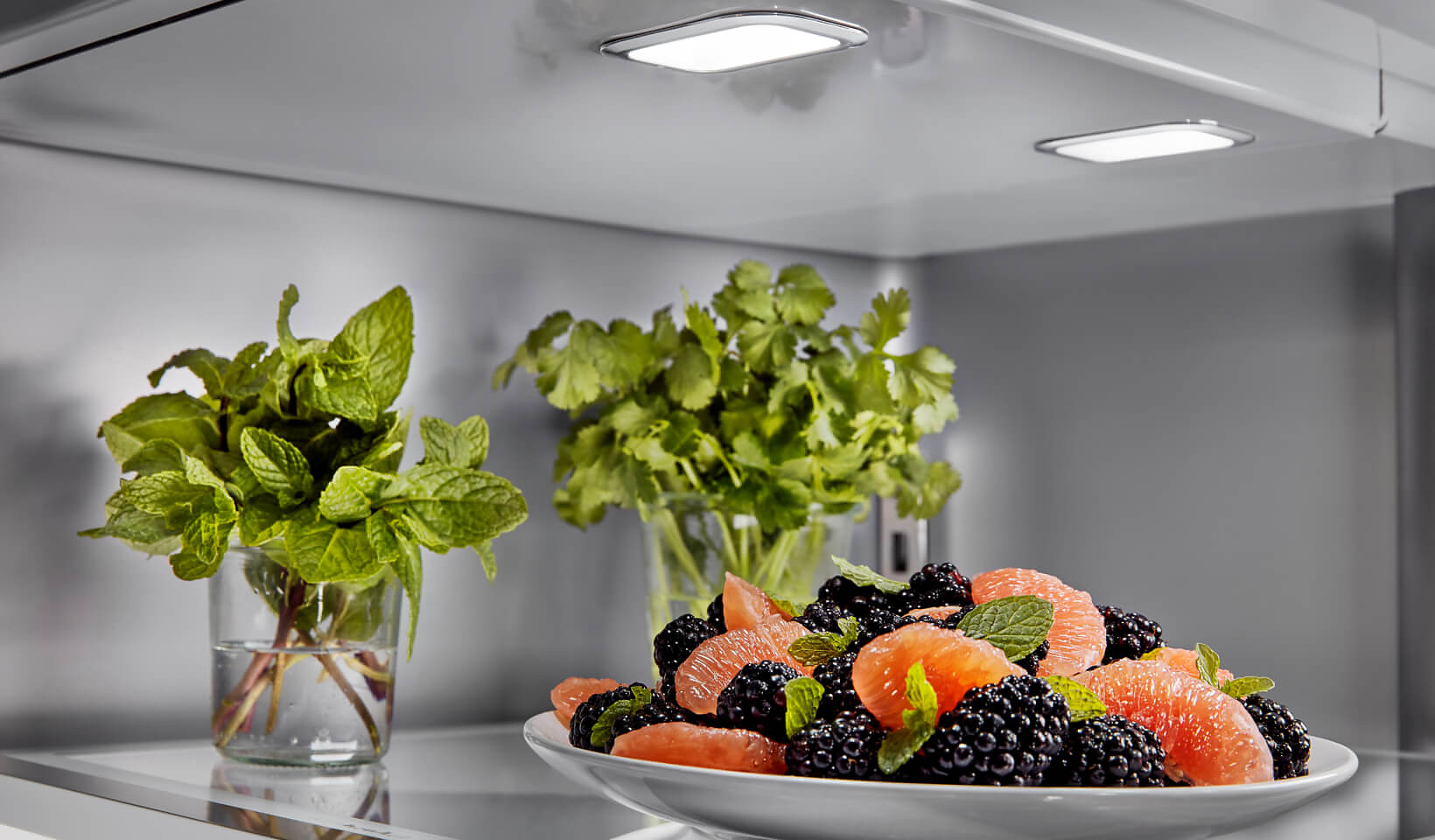 The top shelf of a KitchenAid® French Door Bottom Mount Refrigerator filled with fresh fruit and herbs.