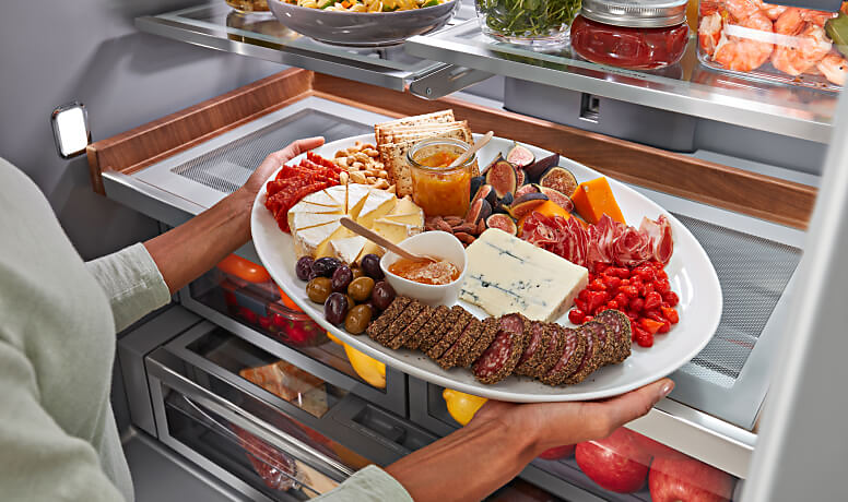 A person placing a charcuterie board on the Premium Wood-Look Finish Sliding Storage Tray. 