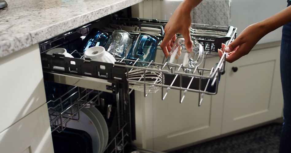 Une personne qui remplit le panier de troisième niveau d'un lave-vaisselle.