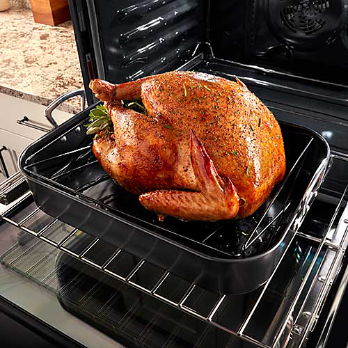 A whole turkey in a roasting pan on a pulled out rack of a Maytag oven