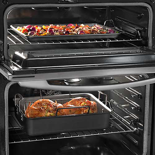 A Maytag double oven. In the top oven with the door opened is a pan of vegetables. In the bottom oven are two roasting chickens in a pan