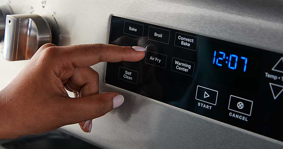 Someone presses a button on the control panel of a Maytag oven. The time reads, "12:07"