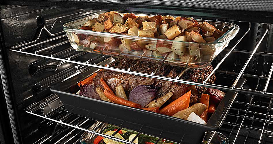 Two racks inside a Maytag oven. On the top rack is a pan filled with potatoes. On the bottom rack is a pan with chicken, onions, carrots and potatoes