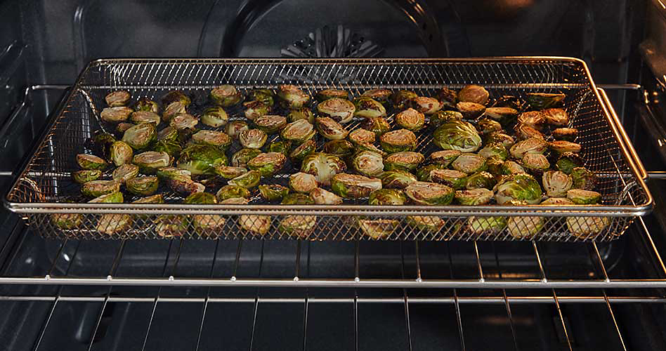 Brussels sprouts cook in a fry basket on a rack in a Maytag oven.