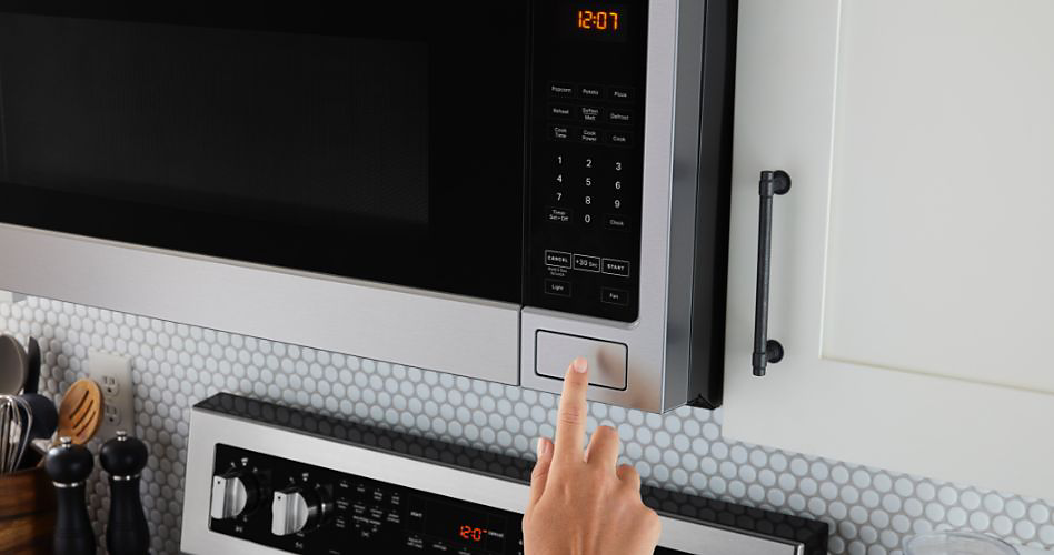 Someone presses the button on a Maytag over-the-range microwave to open the door. Below, the control panel of the Maytag oven is visible. Next to the oven are salt and pepper shakers and a container of kitchen utensils