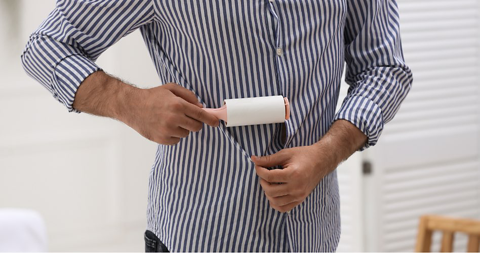 A person wearing a white and blue striped shirt pulls their shirt down so that they can remove lint with a lint roller