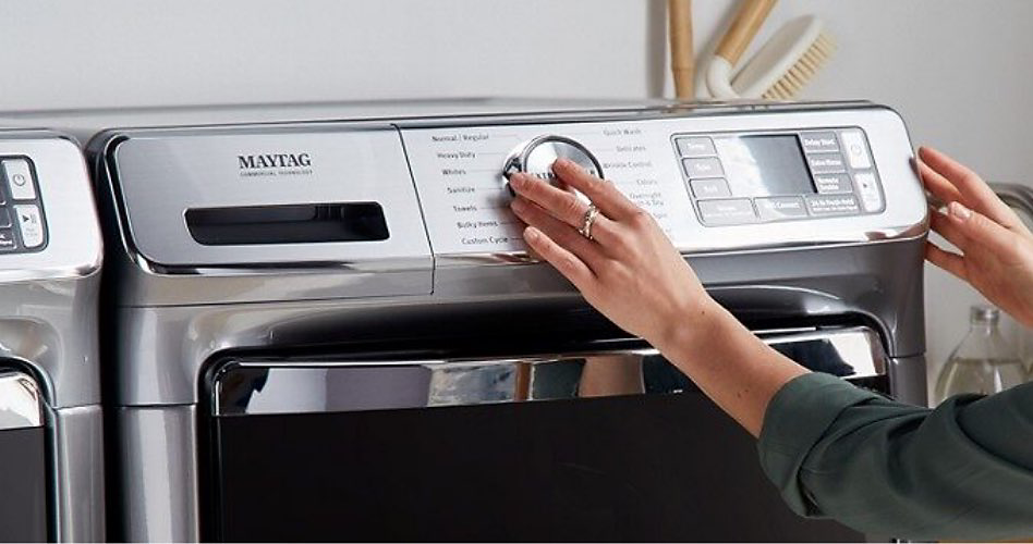 A hand turns the cycle selector on a laundry appliance
