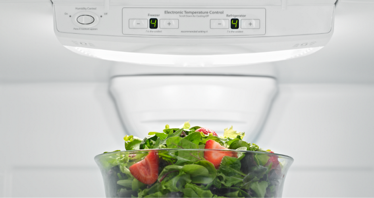 Inside a Maytag Refrigerator. A bowl of salad with strawberries is on a shelf.