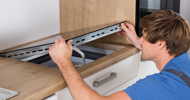 A technician installs a cooktop within a cabinet