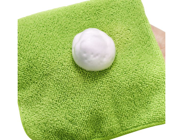  A hand holds a green microfibre cloth with some white foamy cleaner on it. 