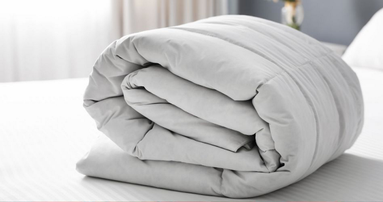 A grey blanket rolled up on a bed with white sheets.