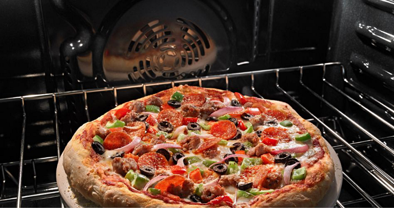 A pizza with olives, green peppers and pepperoni cooks inside a Maytag Oven. 