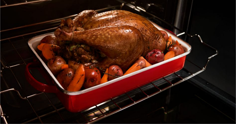  On a rack inside a Maytag Oven, a chicken cooks with potatoes and carrots in a baking dish. 