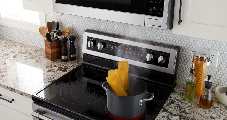 A Maytag Oven with an Over-the-Range Microwave. Lasagna sheets in a pot boil on the stovetop. On the surrounding counters are salt and pepper shakers, a container of kitchen utensils, a glass container of pasta and oil containers. 