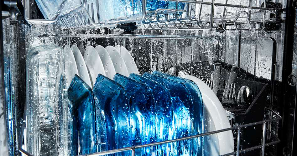 Inside a Maytag Dishwasher. It's mid-wash cycle and filled with plates, glasses and cutlery.