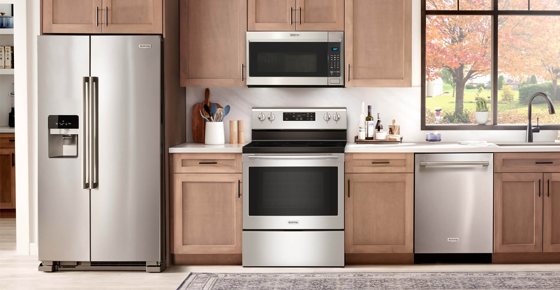 The Maytag® Performance Lineup refrigerator, over-the-range microwave, freestanding electric range and dishwasher in a kitchen with light brown cabinets
