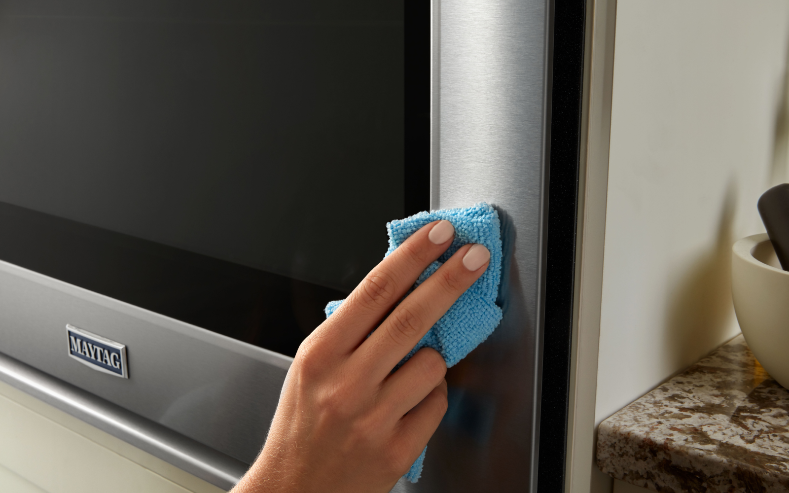 A person wipes down the stainless steel exterior of a Maytag® oven.