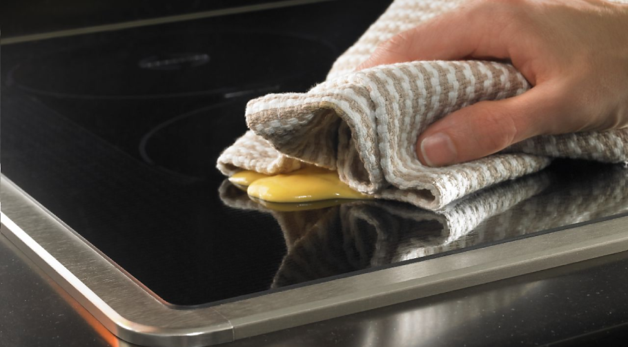 A person wipes the surface of a KitchenAid®  induction cooktop with a cloth.